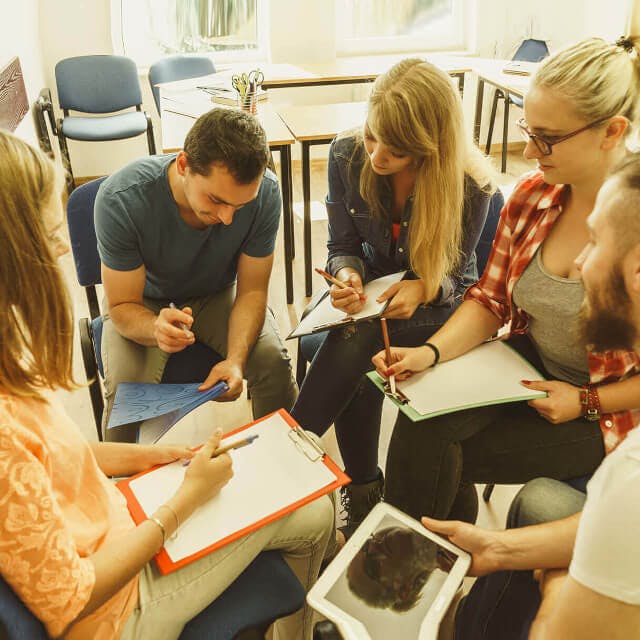 Grupo de estudantes fazendo reunião com prancheta nas mãos