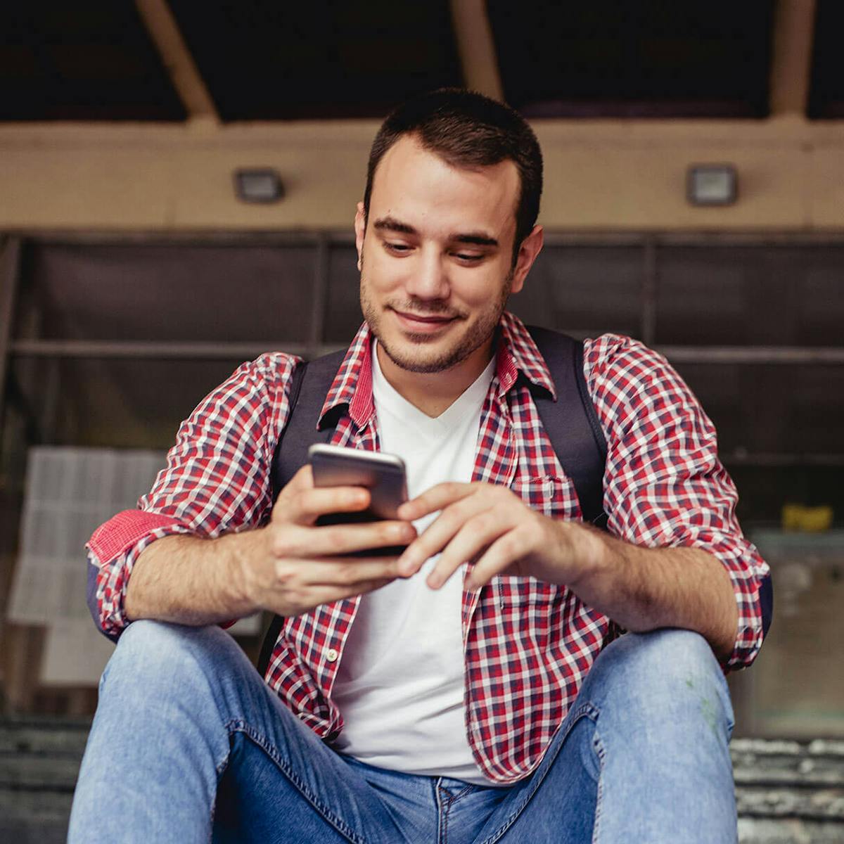 Estudante sentado na escadaria mexendo no seu celular